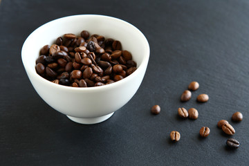 Coffee beans in a white bowl on slate