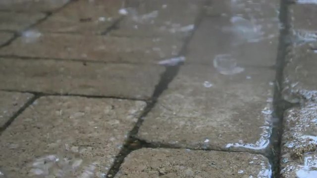 Loop of Rain drops fall into a puddle covering a stone patio