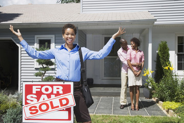 African American real estate agent and couple in front of new house