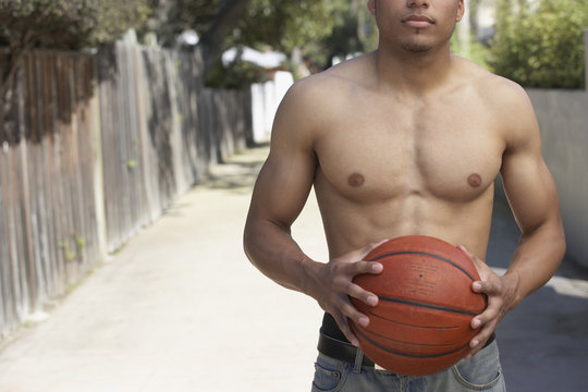 Young mixed race man with bare chest holding basketball