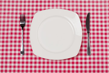 Empty plate setting with plate, knife and fork on red gingham 