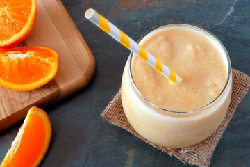 Orange smoothie in a glass with striped straw and fruit slices