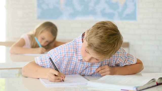 12-year-old boy in classroom writing on notebook