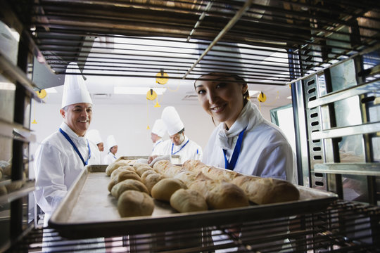 Asian female baker taking tray of bread off rack