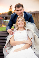 portrait of handsome groom hugging beautiful bride sitting on be