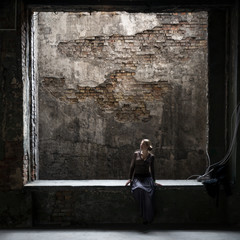 Grungy photo of lonely woman sitting at window in old building