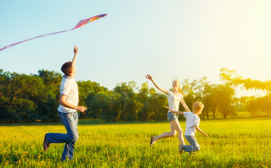 Dad, mom and son child flying a kite in summer nature