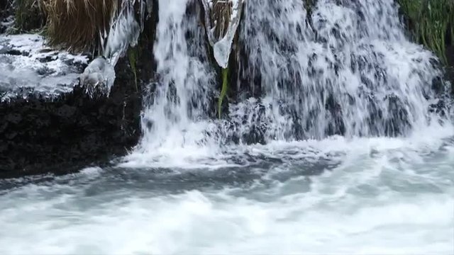 Water flows down frozen rocks and grass into the river