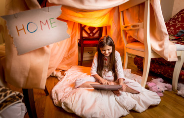 Obraz na płótnie Canvas Cute girl sitting on floor at bedroom and using digital tablet
