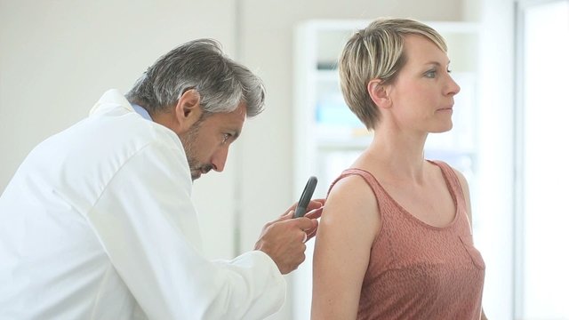 Dermatologist looking at woman's mole with magnifier