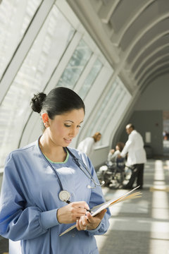 Hispanic nurse reviewing medical chart in corridor