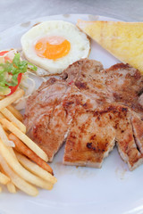 Grilled steaks, French fries, fried egg and vegetables