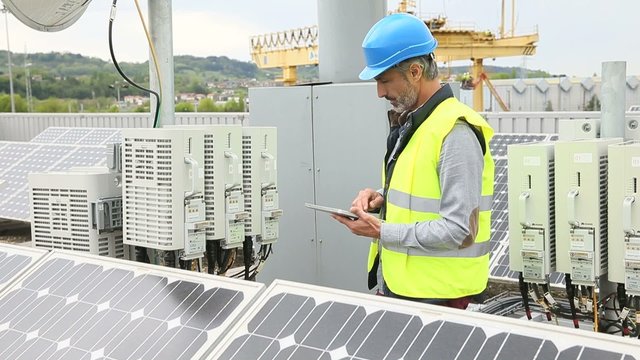Mature engineer on building roof checking solar panels