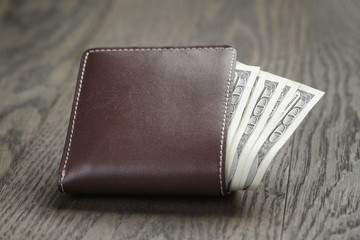 leather wallet on wood table with dollar bills