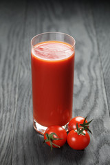 glass of tomato juice on wooden table with tomatoes