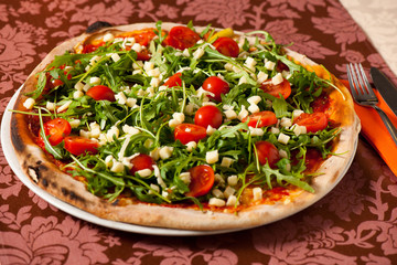 Pizza with rucola and cherry tomatoes on a teble of italian rest