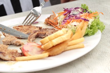 steaks and vegetable salad with french fries.