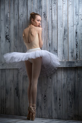 Modest ballerina standing near a wooden wall