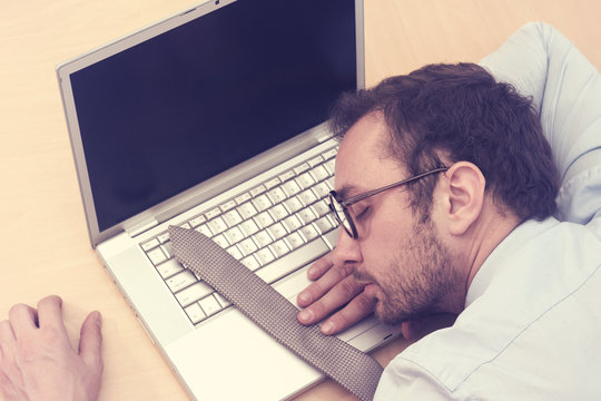 Businessman sleeping on laptop with his tie over keyboard 