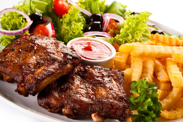 Grilled ribs, French fries and vegetables on white background
