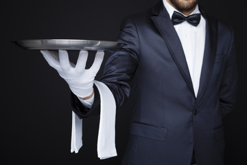 Waiter holding an empty silver tray against dark background