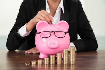 Businesswoman Inserting Coin In Piggybank At Desk