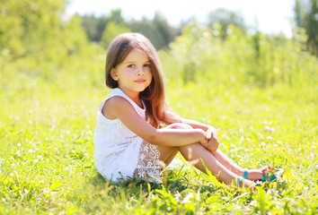 Sunny portrait of beautiful little girl sitting on the grass in