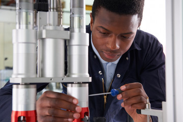 Male Apprentice Engineer Working On Machine In Factory