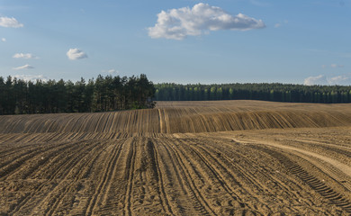Fototapeta na wymiar Furrows in plowed field in hilly terrain in spring - landscape
