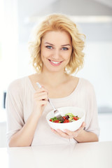 Young woman eating salad in the kitchen