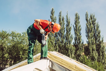 roofer using a drill is fastening a cap to a house roof