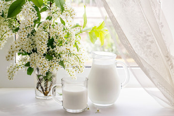 Bouquet of bird cherry and milk on the window