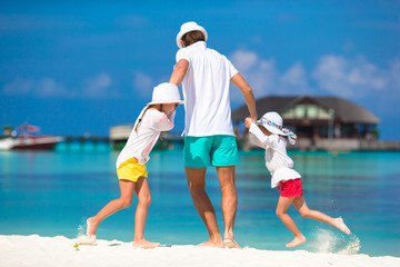 Fototapeta na wymiar Happy dad and adorable little girls at tropical beach having fun