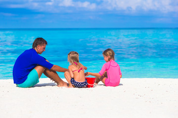 Adorable girls and happy father playing with beach toys on