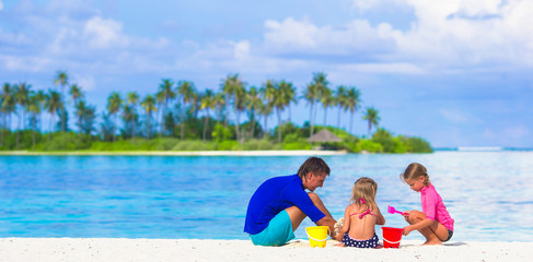 Adorable little girls and dad playing with beach toys on summer