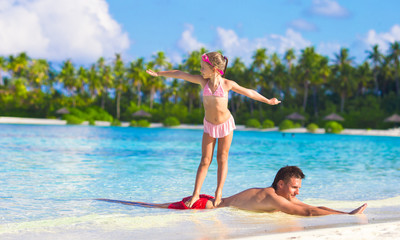 Father with little daughter at beach practicing surfing position