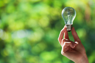 Hand holding light bulb on green nature background with space fo