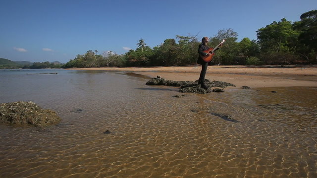 guitarist plays masterly on rock at beach for blonde girl	