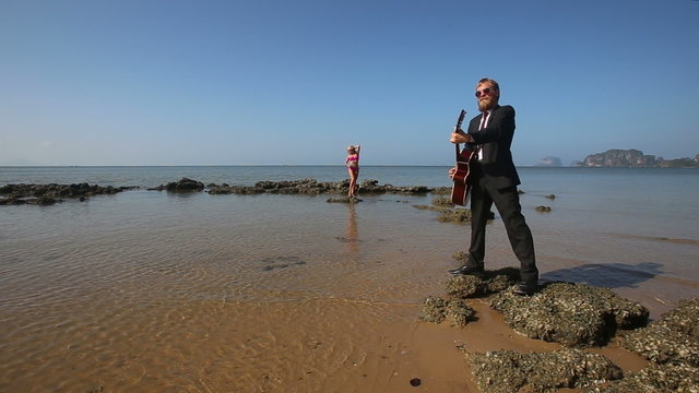 guitarist plays masterly on rock at beach for blonde girl	