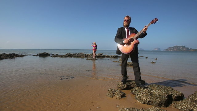 guitarist plays masterly on rock at beach for blonde girl	