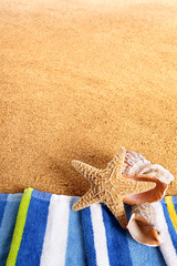Starfish and seashell on a summer beach sand background border with sunbathing towel photo space for copy text vertical
