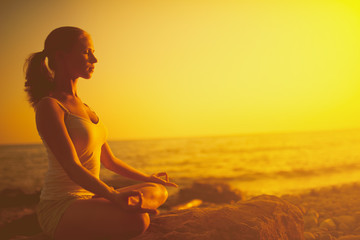 woman meditating in lotus pose on the beach at sunset