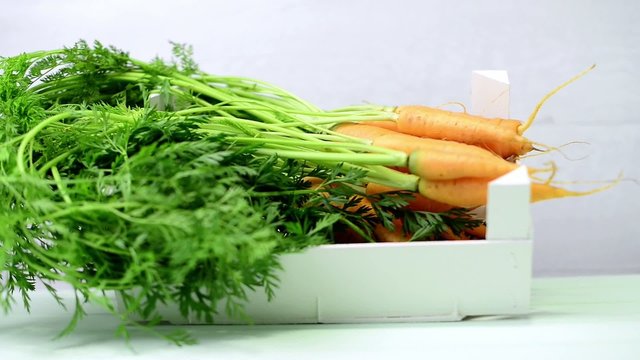Carrots inside white wooden box on the light green wooden table.