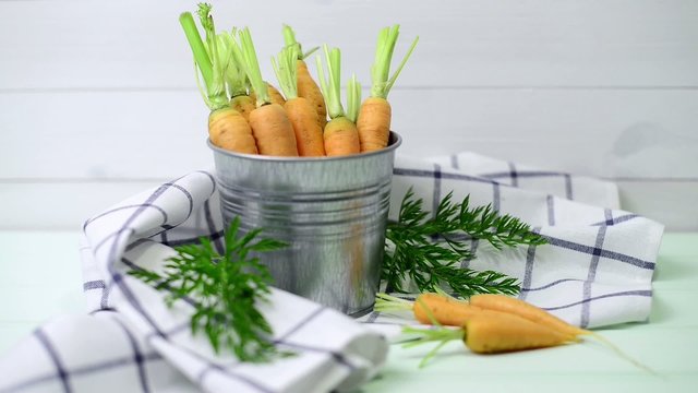 Carrots inside a metal bucket on the light green wooden table.