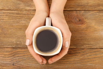 Female hands holding cup of coffee on wooden background