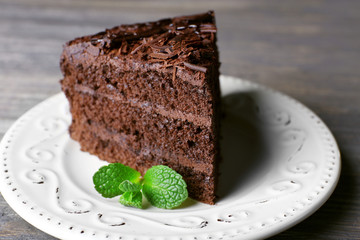 Delicious chocolate cake in white plate with mint on wooden table background, closeup