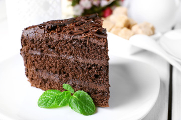 Piece of delicious chocolate cake in plate on color wooden table background