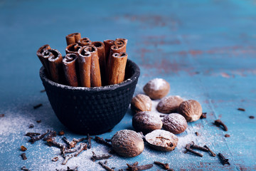 Cinnamon sticks in bowl, nutmeg and cloves on color wooden table background