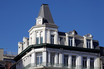 Immeuble ancien avec toit gris en coin de rue, ciel bleu.