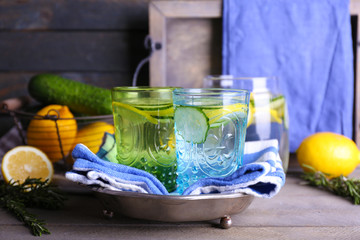 Fresh water with lemon and cucumber in glassware with napkin on wooden background